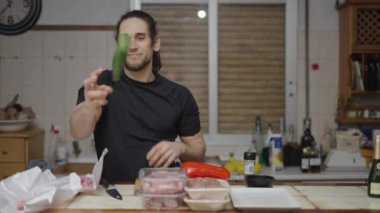 Good looking young man cutting peppers to make diner for friends at home - 4K Horizontal video