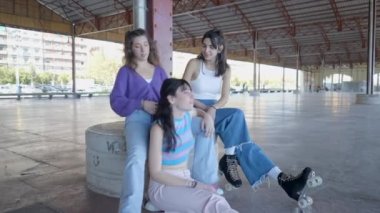 Three girls sit in roller skates and talk as one fixes another hair - 4K Horizontal video