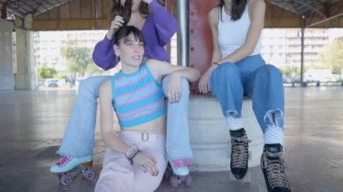 Girls in roller skates sit and talk outdoors, one fixes another hair - 4K Horizontal video