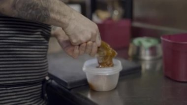 Male chef hands move brown food from plastic bag to small container - 4K Horizontal video