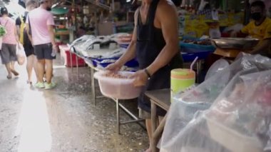 Thai man with cigarette on his mouth shaking a bowl of peanuts in Bangkok market - 4K Horizontal video