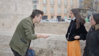 Magician man showing street magic trick with cards. Two girl are enjoying the magic trick in the corner of the street. - 4K Horizontal video