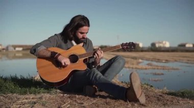 Man playing the guitar sitting in rural area on Valencia, Spain in slow motion - Horizontal video