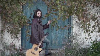 Long haired man looking at the camera while holding a guitar in slow motion - Horizontal video