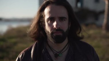 Close up of good looking singer looking at the camera with serious expression, rack focus of palms in background - Horizontal video