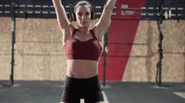 Athletic woman vigorously lifting barbell at the gym while listening to music on headphones - Horizontal video