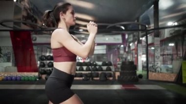 Young woman warming up before exercising in big gym plenty of dumbbells - Horizontal video