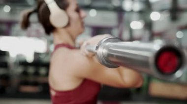 Woman lifting barbell at the gym wearing headphones - Horizontal video