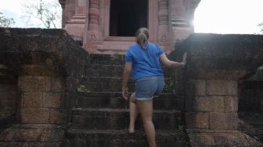 A Woman Tourist Climbing Steps Barefoot Entering The Historical Shrine In Ancient City Museum Park, Samut Prakan Province Outside Bangkok, Thailand. - Low-Angle Shot - 4K Horizontal video