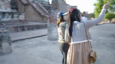 Thai girls sightseeing around Wat Yai Chai Mongkhon temple walking by Buddha stony statues in Ayutthaya, Thailand - 4K Horizontal