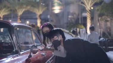 A couple was looking at a red car which was parked on the side of a road. They were amazed to see that car and clicking picture of that car by their mobile - 4K Horizontal video
