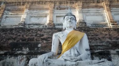 Ancient, hand-carved yellow cloth Buddha sculpture on brick steps at Wat Yai Chai Mongkhon in Ayutthaya, Thailand. - 4K Horizontal