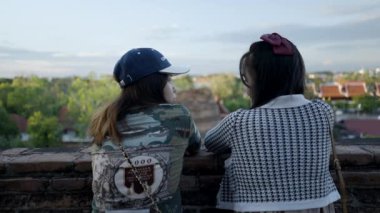 Happy Thai girls talking on a high-ground terrace of a Wat Yai Chai Mongkhon temple in Ayutthaya with a city skyline , Thailand - back view - 4K Horizontal