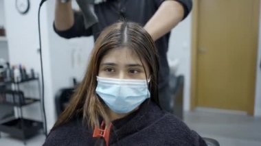 Hairdresser drying clients hair wearing a face mask for COVID-19 prevention - 4k Horizontal video