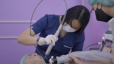 Asian doctor performs skin lifting with laser device on caucasian man - 4K Horizontal video
