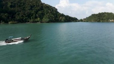 Thai traditional long-tailed hopping tour motorboat traveling along the Railay peninsular on sunny day, Krabi, Thailand - Aerial side tracking flight - 4K Horizontal video