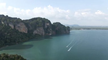 Aerial view of Railay Beach in Krabi on the Railay Peninsula with two hopping tour tourist boats traveling in the sea on a cloudy day - 4K Horizontal video