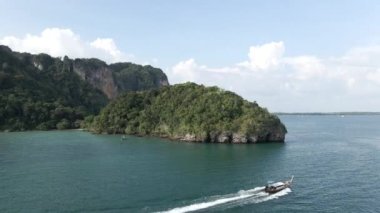 Small hopping tour boat traveling along the Railay peninsular isle coastline in Krabi province of Thailand - Aerial tracking shot - 4K Horizontal video