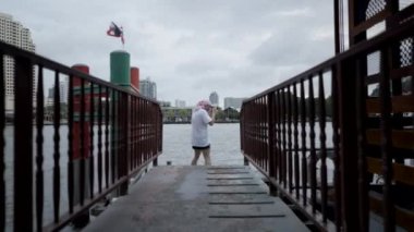 DSLR kameralı erkek turist Tayland 'da Chao Phraya Nehri' nin karşısındaki Bangkok Şehri 'nin panoramik fotoğrafını çekiyor. geniş, doli-in çekim - 4K Yatay video