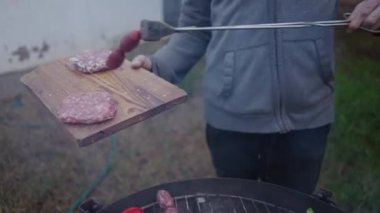 Kimliği belirsiz bir adam mangalda sosis ve burger pişiriyor. Ağır çekim. 4K yatay görüntü.