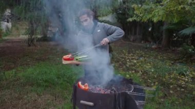 Genç İspanyol adam ormandaki bahçe evinde sebze pişiriyor. 4K Yatay Video.