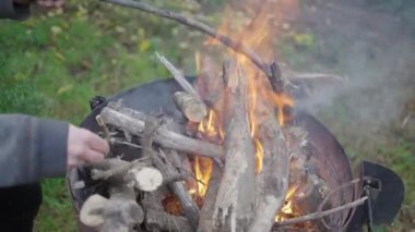 Yüzsüz adam dışarıda odun pişirip barbekü yapmak için yangın çıkarıyor. 4K yatay video.
