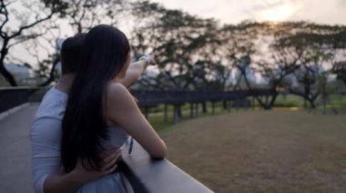 Köprüde duran yüzsüz çift Benchakitti Bangkok parkındaki manzarayı inceliyor - 4K Yatay Klip