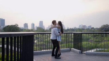 Kucaklaşan ırklar arası bir çift. Adam kadını kaldırır ve döndürür. Benchakitti parkındaki şehir bakış açısı - 4K Yatay Klip