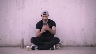Hipster kaykayda oturan adam akıllı telefon kullanarak selfie çekiyor - 4K Yatay Video