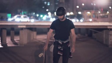 Gece kentinde kaykay tutan bir resim için poz veren kaykay modeli - arka planda ışıklar - 4K yatay video