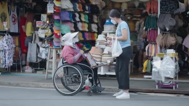 タイのバンコクのチャトゥチャック通り市場では 車椅子の障害者の女性が女性に製品を販売しています 4K水平ビデオ — ストック動画
