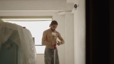Çekici hippi adam boya silindiri ve beyaz boya kullanarak tavanı boyuyor. 4K yatay görüntü.