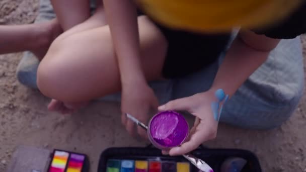 認識できない女性は ブラシを構成する紫色のボディペイントを混合 ビーチに座っている 青で手描き 4K水平ビデオ — ストック動画