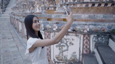 Taylandlı kadının Wat Arun Tapınağı 'nda akıllı telefonuyla selfie çekerken yan görüntüsü. Kadın mutlu bir şekilde gülümsüyor - 4K Yatay Video