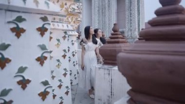 İki Asyalı arkadaş Wat Arun tapınağında gezip manzarayı izliyorlar. Mutlu arkadaşlar birlikte yeni yerler keşfettiler - 4K Yatay video