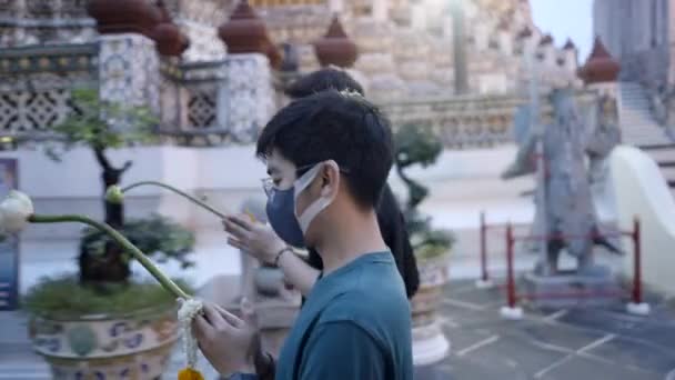 アジア人の男性はお供え物として花を持って仏教寺院を歩く 男性が手をつないでいます 4K水平ビデオ — ストック動画