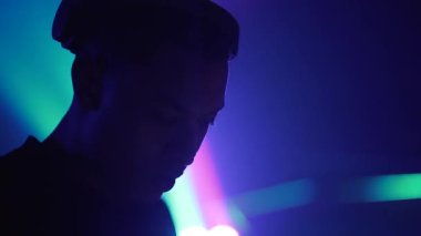 DJ müzik çalıyor ve bardaktan içki içiyor. Arka planda renkli hareket eden ışıklar. - 4K Yatay Görüntü