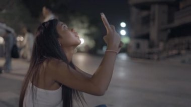 Asyalı kız yerde oturuyor ve çevreyi gözetliyor. Fotoğraf çekmek için telefonu tutuyor. 4K Yatay Video.