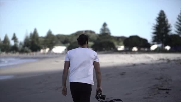 Man Loopt Met Een Camera Zijn Hand Het Strand Van — Stockvideo