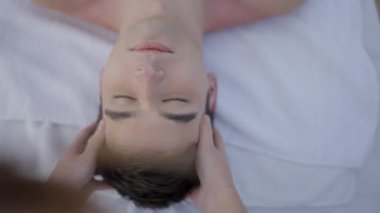 Omuz hizasında, genç oğlanın kafasına masaj yapan bir kadın. Oğlan masaj sırasında rahatlar - 4K Yatay video
