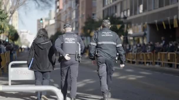 スペインのバレンシアで開催されるサンアントニ フェスティバルでは バリケードフェンスの後ろに立つ人々と一緒に秩序を維持する通りを歩く警察官 4K水平ビデオ — ストック動画