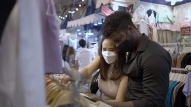 Karışık ırk çifti birlikte alışveriş yapıyor. Çift elbise raflarında farklı tişörtler okuyor - 4K Yatay Video