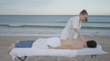 Arka planda deniz dalgaları ve ön planda dikkatsiz masaj yapan kadın - 4K Yatay Video