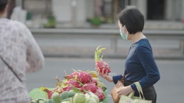 Középkorú Maszkban Sárkánygyümölcsöt Vásárol Helyi Gyümölcsárustól Aki Bangkokban Thaiföldön Árul — Stock videók