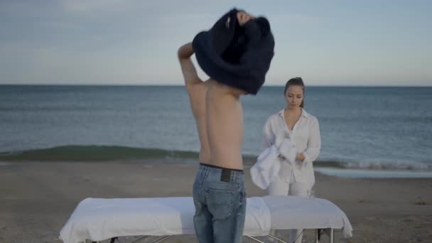 Klient Przybywa Plażę Zdejmuje Sweter Masaż Masażystka Ubrana Biało Poziome — Wideo stockowe
