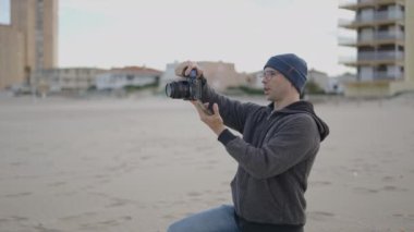 Kafkasyalı fotoğrafçı bir kış sabahı plajda fotoğraf çekimi yapıyor, müşterisiyle elinde kamera ile konuşuyor - 4K Yatay Video