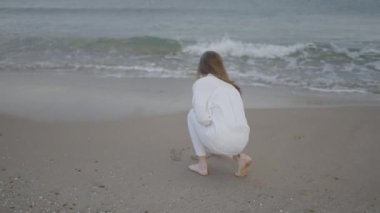 Tanınmayan bir kadının arka planda kalan görüntüsü kuma kelimeler yazıyor. Arkaplanda plaj dalgaları - 4K Yatay video