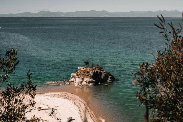 上に少し植生と穏やかな海で山を見下ろす白い砂浜の海岸に石と岩の小さな好奇心の島 ラベルタスマンビーチ 新しいニュージーランド 4K水平線 — ストック写真