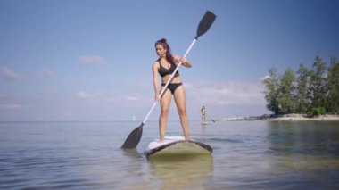 Tayland sahilindeki kameraya doğru kürek çeken çekici bir kadın. Ağır çekim. 4K yatay video.