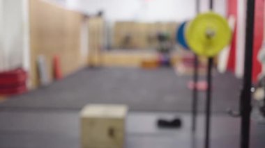 Güçlü bir kadın, spor salonunda bacak kaldırıyor. Spor aletlerinin odaklanmamış arkaplanı - 4K Yatay Video
